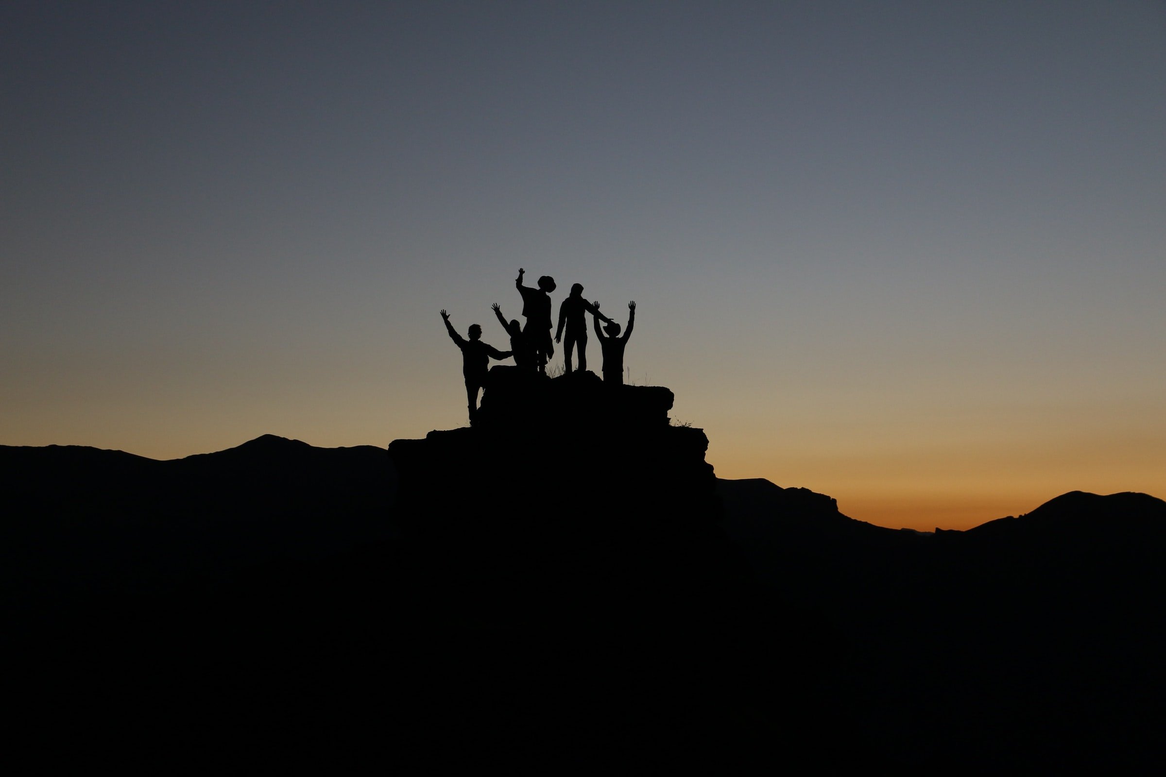 Silhouette of a group of people standing on atop a mountain