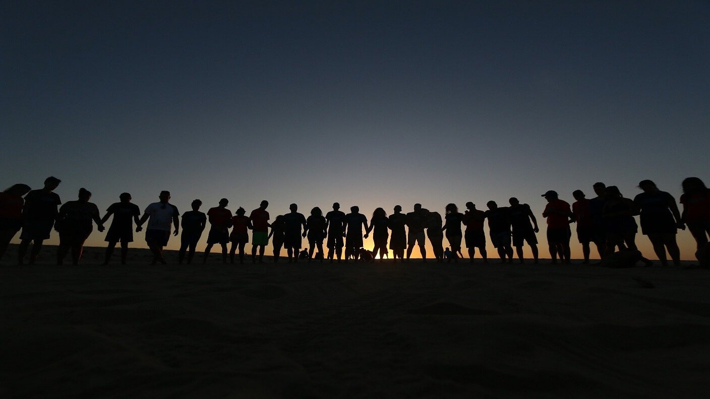 silhouette of a group of people standing in a line in front of the sun