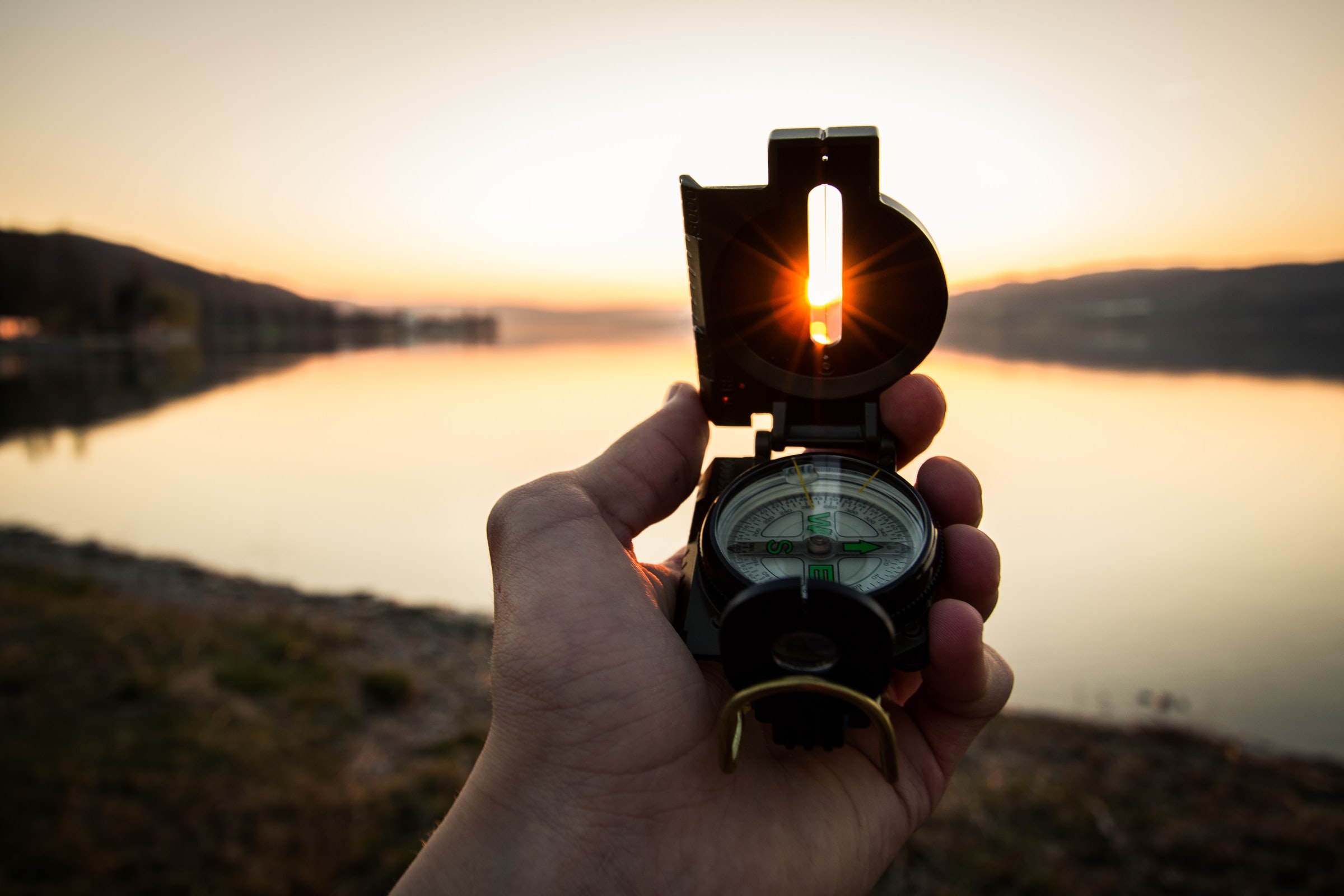 person holding a compass in front of the setting sun